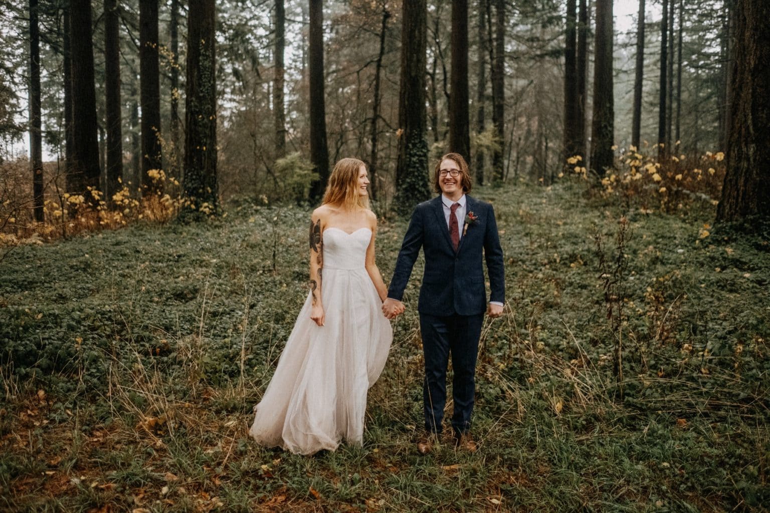bride in boho wedding dress holding hands with groom in foggy forest